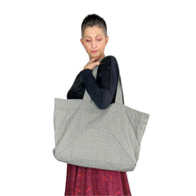 Load image into Gallery viewer, Kulmi Bag sewing pattern by Dhurata Davies – worn on left arm, made in light denim with dark stripes, showing front triangular pocket detail.