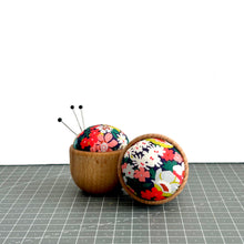 Load image into Gallery viewer, a handmade pincushion in liberty fabric on a wooden base, three pins on it, and one pincushion on its side to show the cute floral fabric, thorpe