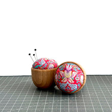 Load image into Gallery viewer, a handmade pincushion in liberty fabric on a wooden base, three pins on it, and one pincushion on its side to show the cute floral fabric, strawberry thief