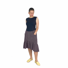 Load image into Gallery viewer, Olive skirt sewing pattern, View D — front view of mid-length tiered skirt with ruffle and curved high-low hem, left hand in integrated front pocket, made in dark plum fabric with white polka dots