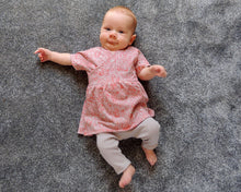 Load image into Gallery viewer, flo dress and riley leggings sewing pattern for babies and toddlers by dhurata davies, lovely baby laying on the floor, wearing the flo dress and riley leggings