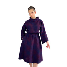 Load image into Gallery viewer, Edith sewing pattern – mid-length linen dress with elasticated waist, long wide sleeves, and funnel neck, front view in plum and navy checkered fabric, model with right hand in pocket