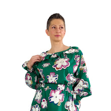 Load image into Gallery viewer, Edith sewing pattern – bodice view of dress with frilled neckline, frilled cuffs, and elasticated waistband, big floral print on green background, right hand touching frill