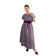 Load image into Gallery viewer, Edith sewing pattern – long sleeveless linen dress with elasticated waist and curved hem, front view with left foot forward, model touching neckline, styled with a contrast quilted belt