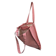 Load image into Gallery viewer, twin tote, bag sewing pattern by dhurata davies, side view, hanging from one handle, showing the inside structure of the bag compartments. made in a striped red and tan fabric