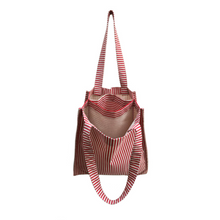 Load image into Gallery viewer, twin tote, bag sewing pattern by dhurata davies, hanging from one handle, showing the inside structure of the bag compartments. made in a striped red and tan fabric