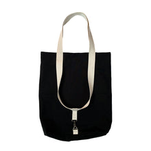 Load image into Gallery viewer, A black canvas tote bag with cream-colored shoulder straps and a silver metal clasp, shown against a plain white background.