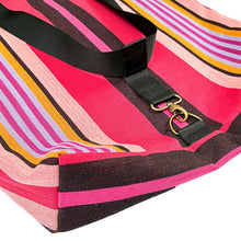 Load image into Gallery viewer, A close-up of a striped tote bag with a vibrant pink, black, orange, and purple pattern, featuring a black webbed strap and a gold-tone metal clasp on a white background.