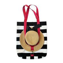 Load image into Gallery viewer, A black and white striped tote bag with bright red handles, featuring a sunhat harness which hangs on the front of the bag.
