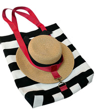 Load image into Gallery viewer, A black and white striped canvas tote bag with bright red handles, shown with a woven straw sun hat harnessed within the strap.
