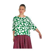 Load image into Gallery viewer, Woman wearing the Rea Top sewing pattern in green and white print, hand extended to show sleeve, styled with a red skirt
