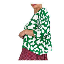 Load image into Gallery viewer, Side view of woman wearing the Rea Top sewing pattern in green and white print, styled with a red skirt