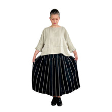 Load image into Gallery viewer, Woman wearing the Rea Top sewing pattern in natural linen with pleated cuffs, styled with a black and beige striped midi skirt
