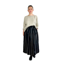 Load image into Gallery viewer, Woman wearing the Tia Skirt sewing pattern in midi length in black fabric with beige stripes, styled with a beige top half tucked in