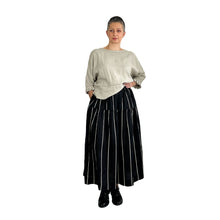 Load image into Gallery viewer, Woman wearing the Tia Skirt sewing pattern in midi length in black fabric with beige stripes, styled with a beige top, one hand on hip one in pocket
