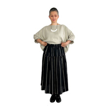 Load image into Gallery viewer, Woman wearing the Tia Skirt sewing pattern in midi length in black fabric with beige stripes, holding the waistband to show the elasticated detail, styled with a beige top