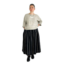 Load image into Gallery viewer, Woman wearing the Rea Top sewing pattern in natural linen with pleated cuffs, styled with a black and beige striped midi skirt, hand on hip
