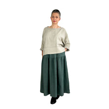 Load image into Gallery viewer, Woman wearing the Tia Skirt sewing pattern in teal in midi length, styled with a natural linen top, hand in pocket