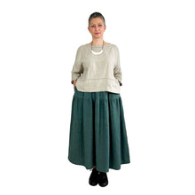 Load image into Gallery viewer, Woman wearing the Rea Top sewing pattern in natural linen, styled with a teal midi skirt, hands in pockets