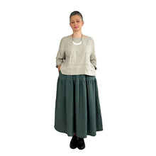 Load image into Gallery viewer, Woman wearing the Rea Top sewing pattern in natural linen, styled with a teal midi skirt, hands in pockets
