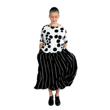Load image into Gallery viewer, Woman wearing the Rea Top sewing pattern in black and white polka dot, styled with a black and white striped midi skirt