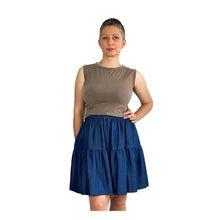Load image into Gallery viewer, Woman wearing the Tia Skirt sewing pattern in blue in mini length, styled with a brown sleeveless top, one hand on hip and one hand in pocket