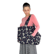 Load image into Gallery viewer, kulmi bag, sewing pattern by dhurata davies, bag worn in left arm, hand reaching inside front triangular pocket, made in light grey canvas fabric with large dark flowers 