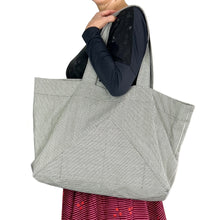 Load image into Gallery viewer, kulmi bag, sewing pattern by dhurata davies, bag worn in left arm, made in light grey canvas fabric with thin dark stripes, highlighting the pocket shape