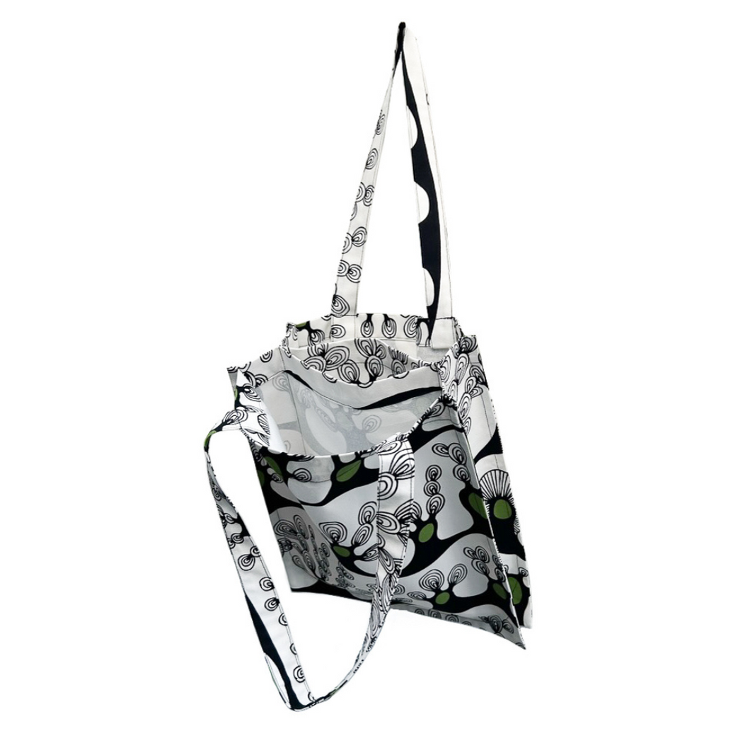 twin tote, bag sewing pattern by dhurata davies, hanging from one handle, showing the inside structure of the bag compartments. made in an abstract tree design on a white background